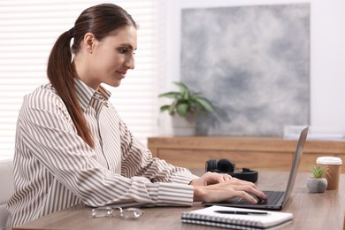 Photo of Programmer working on laptop at wooden desk indoors