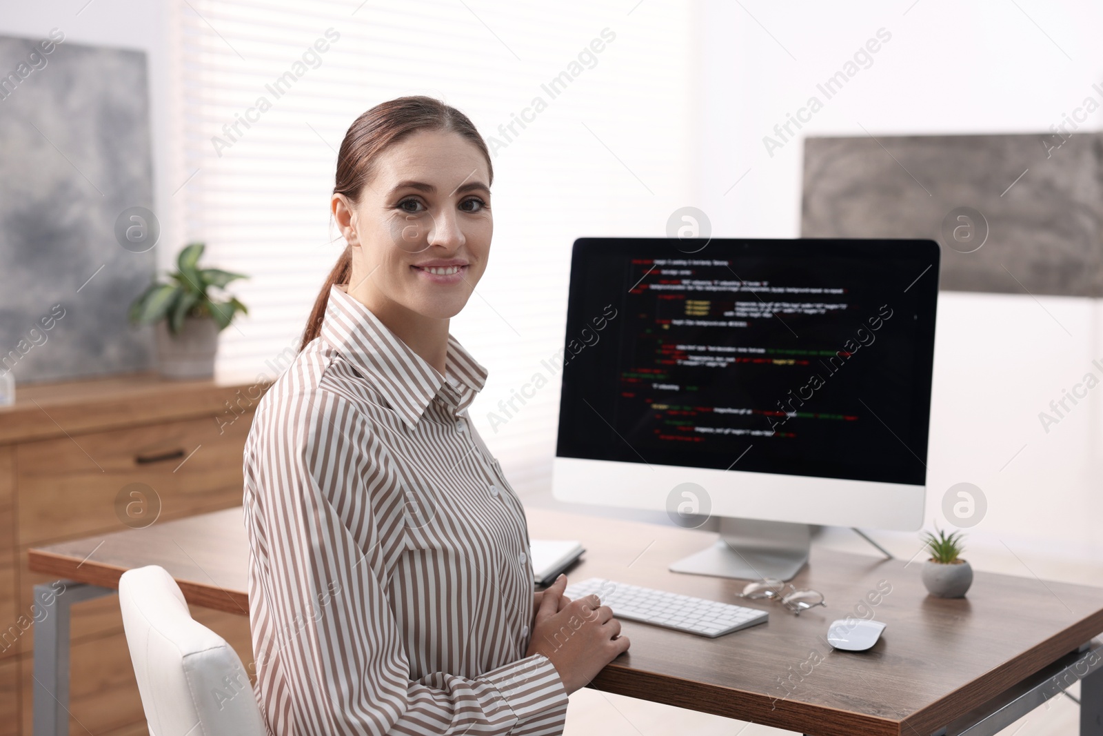 Photo of Programmer working on computer at wooden desk indoors