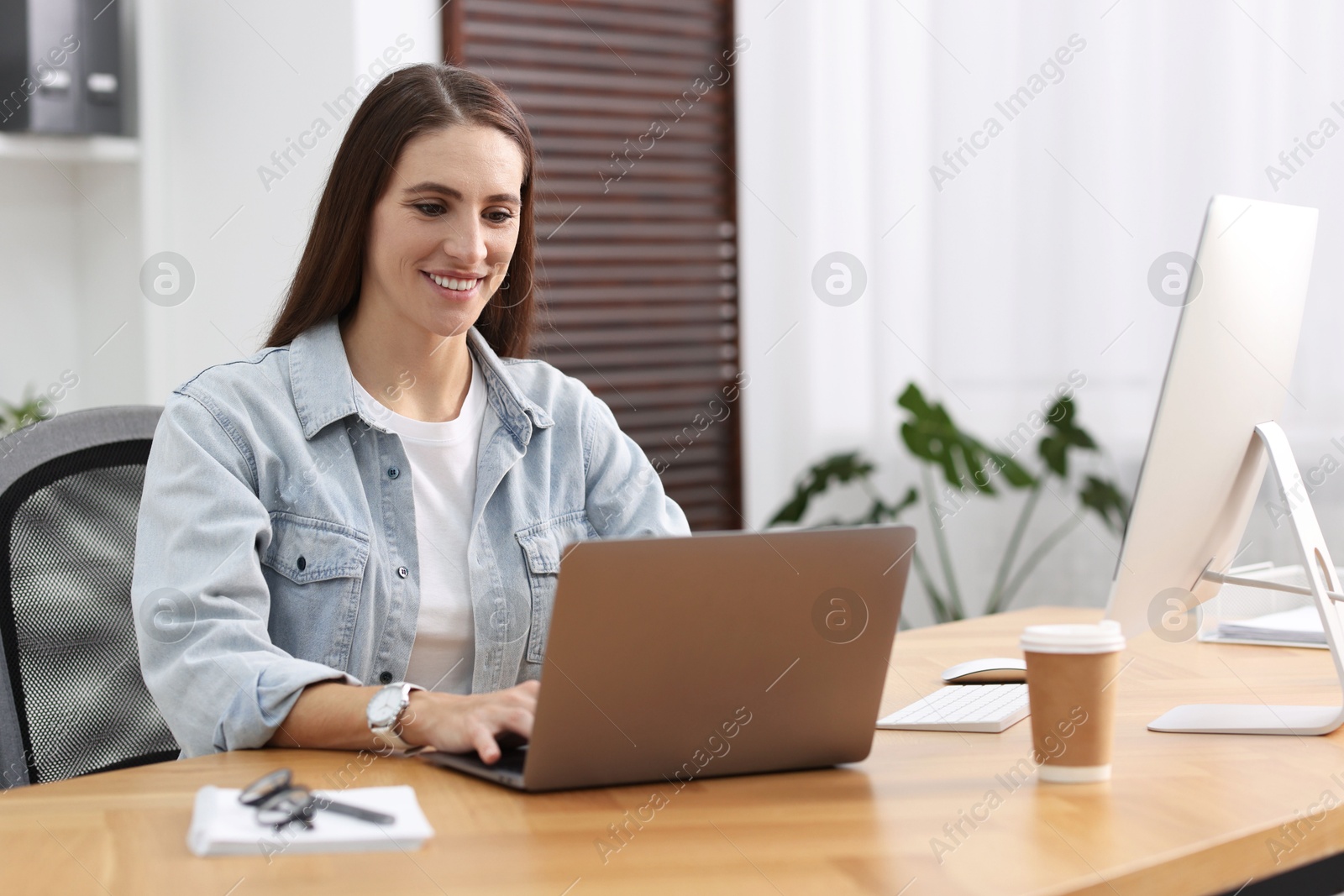 Photo of Programmer working on laptop and computer at wooden desk indoors