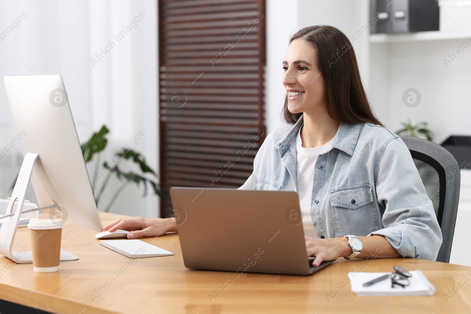 Photo of Programmer working on laptop and computer at wooden desk indoors