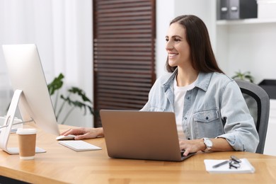 Photo of Programmer working on laptop and computer at wooden desk indoors