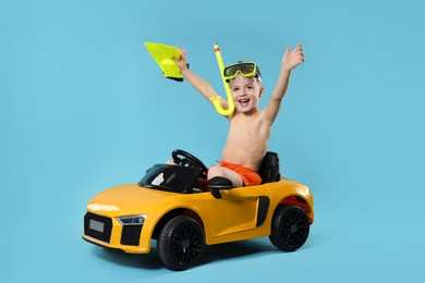 Photo of Cute little boy in beachwear with snorkeling equipment and toy car on light blue background