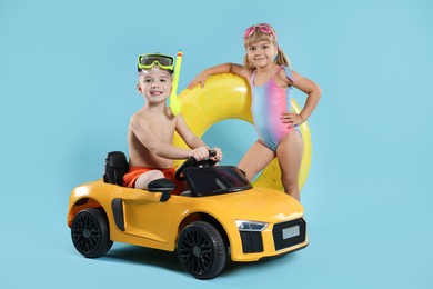 Photo of Cute little kids in beachwear with inflatable ring and toy car on light blue background