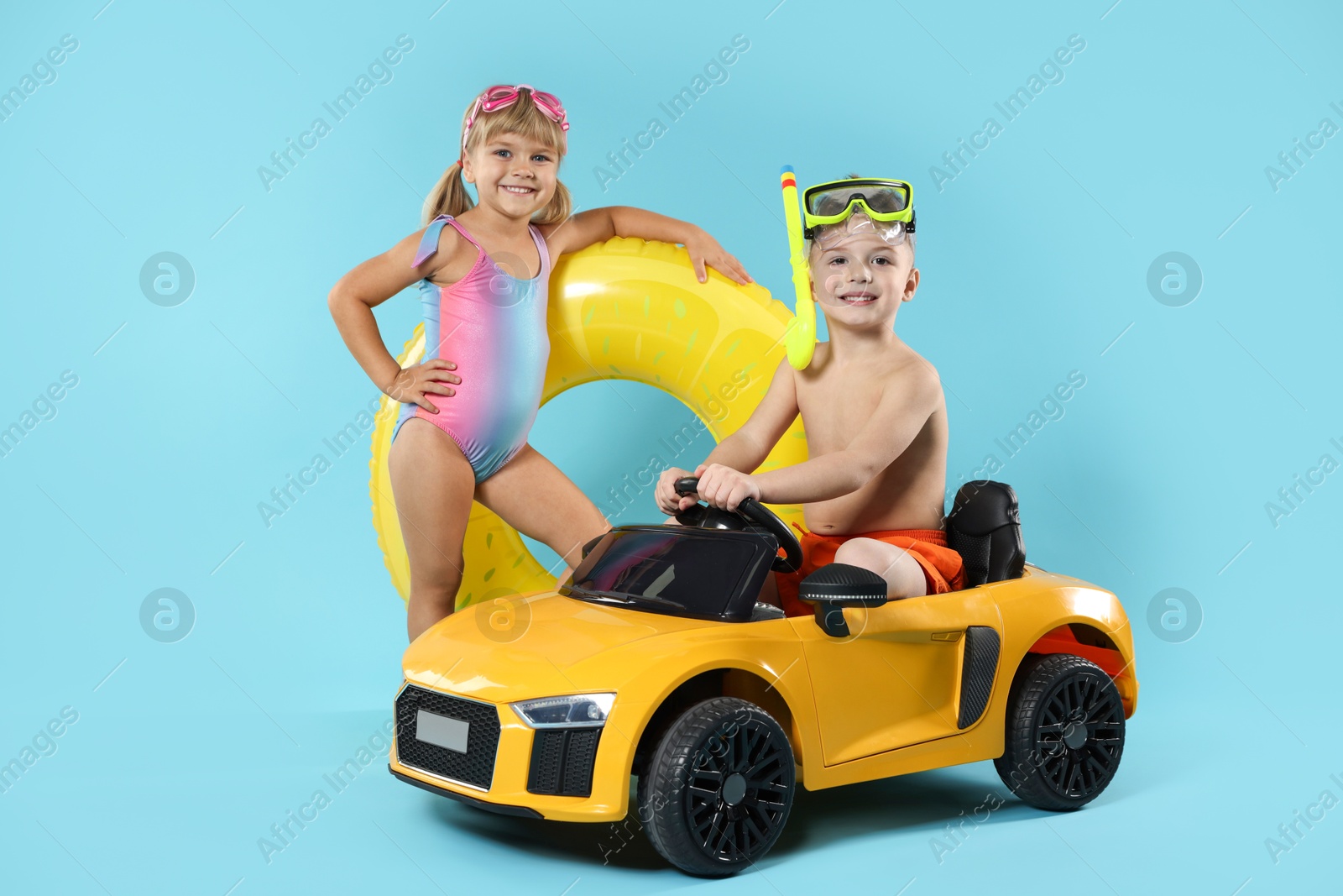 Photo of Cute little kids in beachwear with inflatable ring and toy car on light blue background