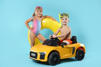 Photo of Cute little kids in beachwear with inflatable ring and toy car on light blue background