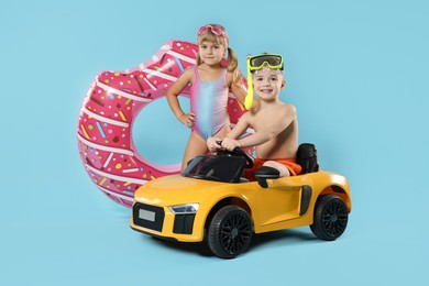 Photo of Cute little kids in beachwear with inflatable ring and toy car on light blue background