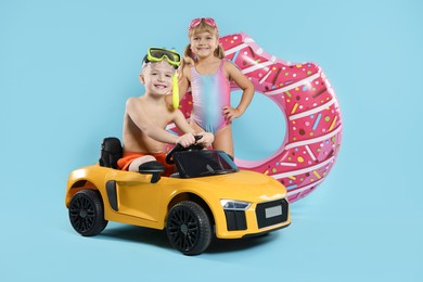 Photo of Cute little kids in beachwear with inflatable ring and toy car on light blue background