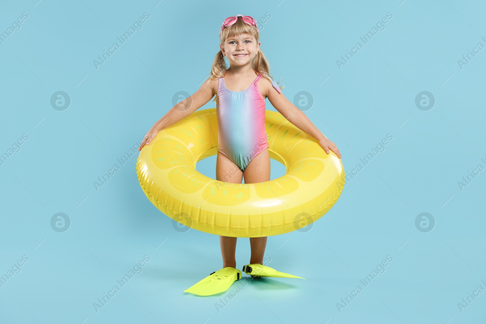 Photo of Cute little girl in beachwear with diving mask, inflatable ring and flippers on light blue background