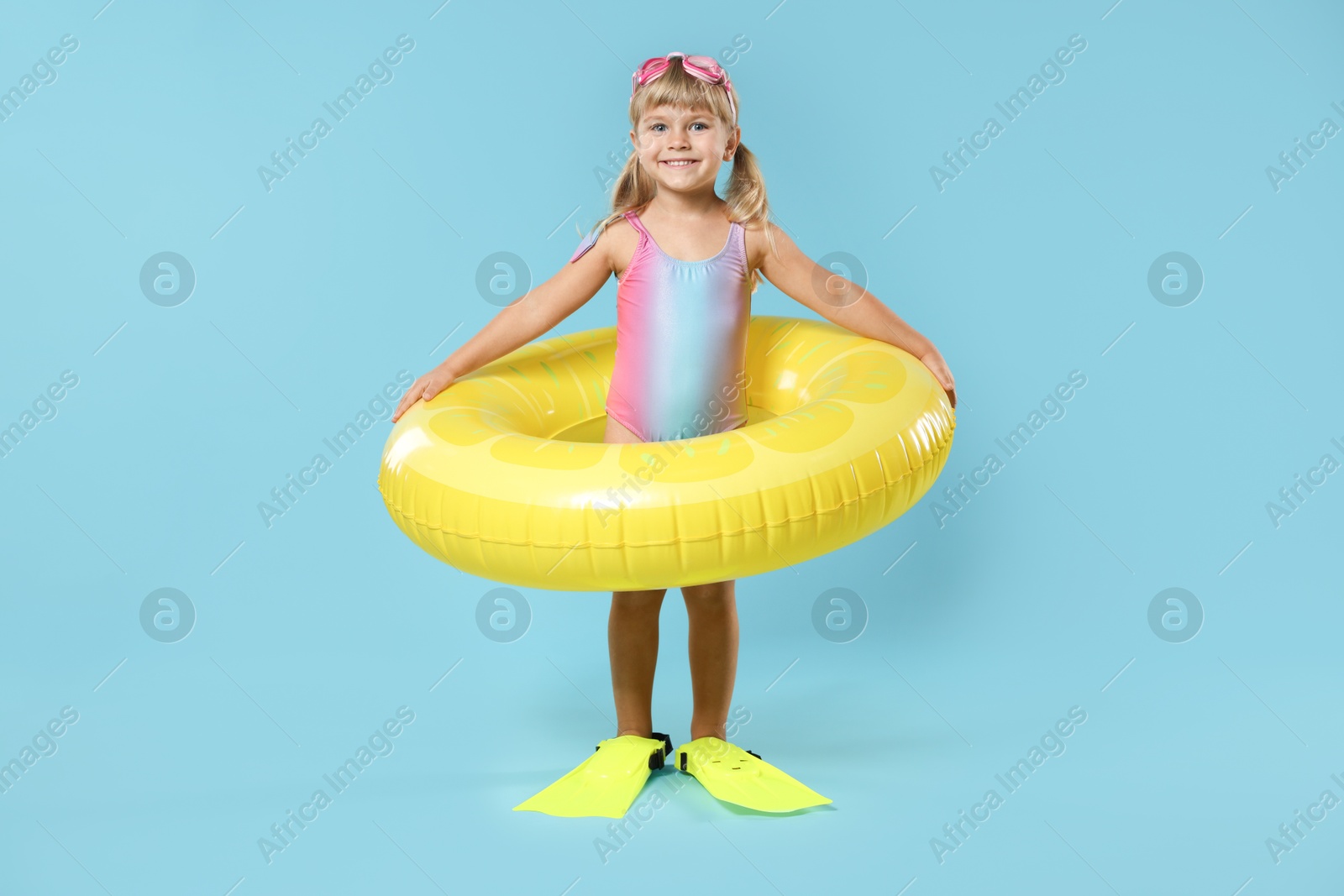 Photo of Cute little girl in beachwear with diving mask, inflatable ring and flippers on light blue background