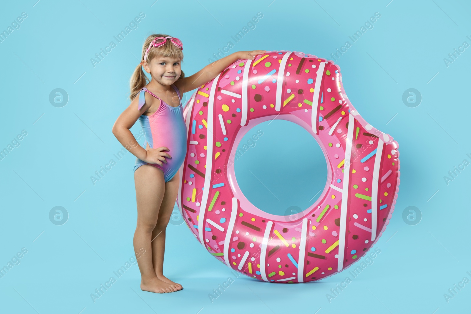 Photo of Cute little girl in beachwear with diving mask and inflatable ring on light blue background