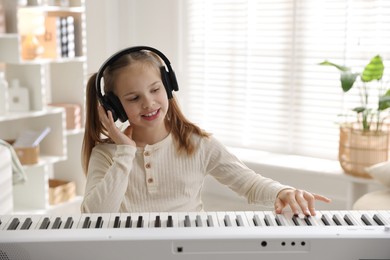 Photo of Cute girl in headphones playing synthesizer at home