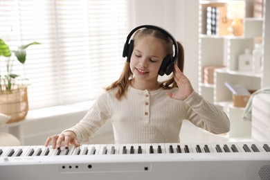 Photo of Cute girl in headphones playing synthesizer at home