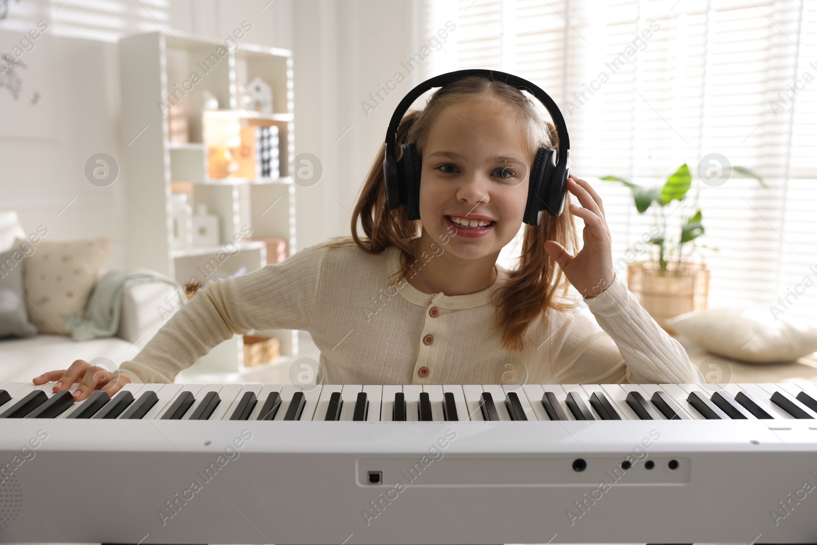 Photo of Cute girl in headphones playing synthesizer at home