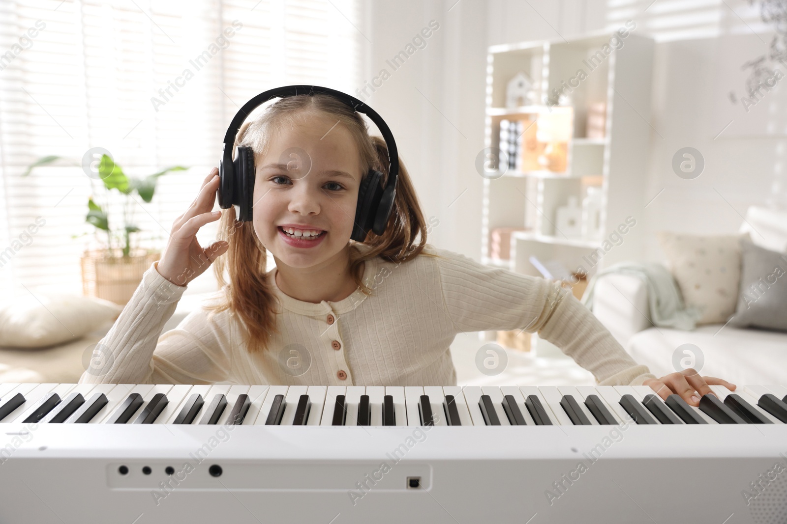 Photo of Cute girl in headphones playing synthesizer at home