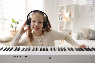 Cute girl in headphones playing synthesizer at home