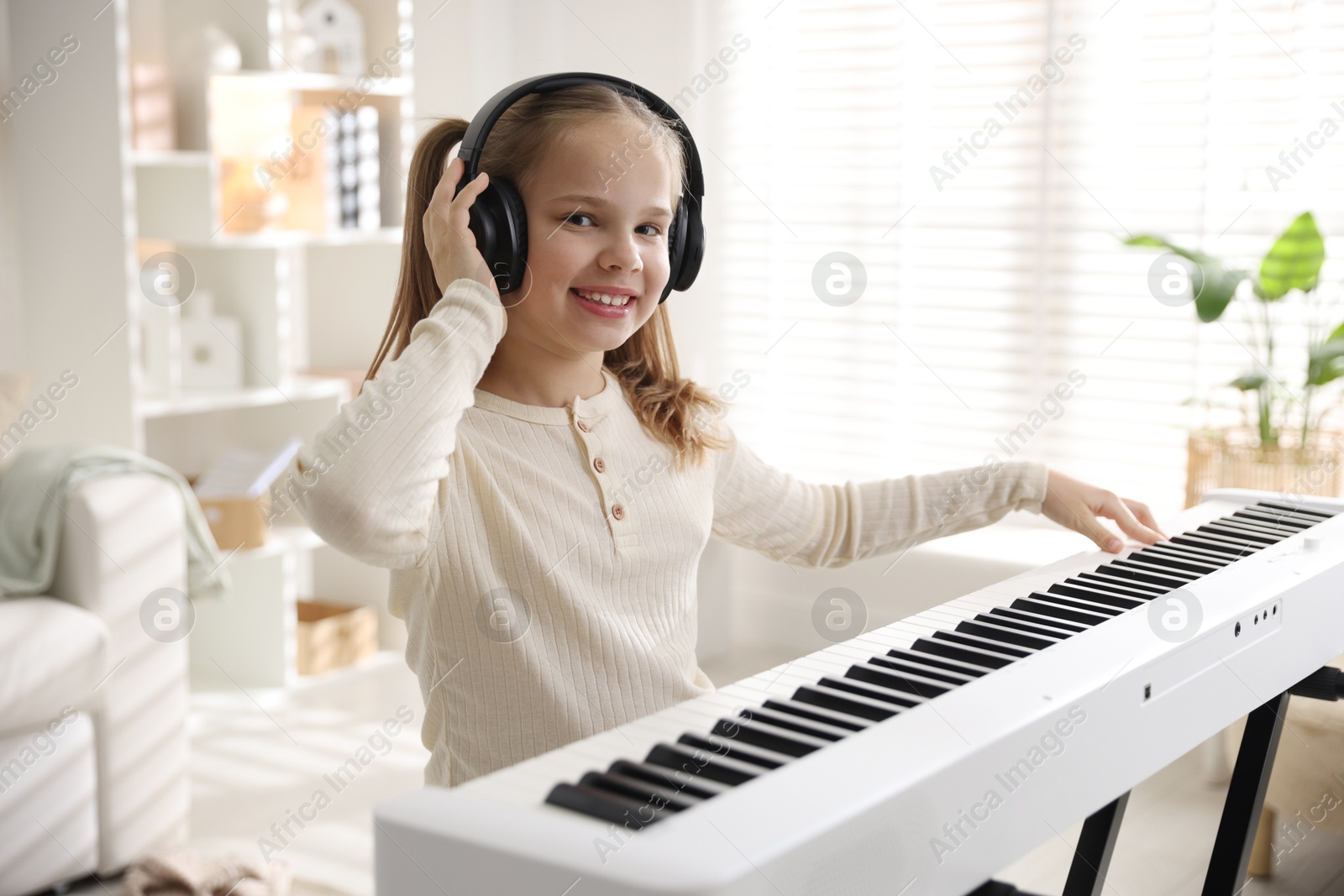 Photo of Cute girl in headphones playing synthesizer at home