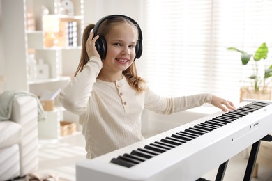 Photo of Cute girl in headphones playing synthesizer at home