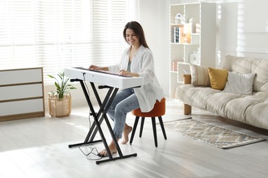 Photo of Smiling woman playing synthesizer at home. Electronic musical instrument