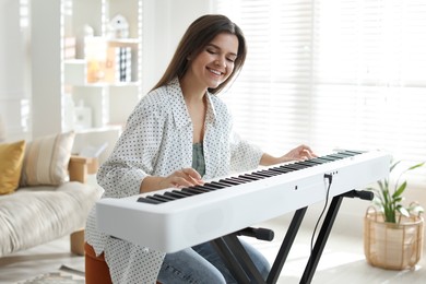 Photo of Smiling woman playing synthesizer at home. Electronic musical instrument