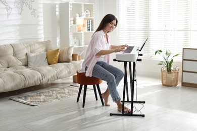 Photo of Smiling woman playing synthesizer at home. Electronic musical instrument