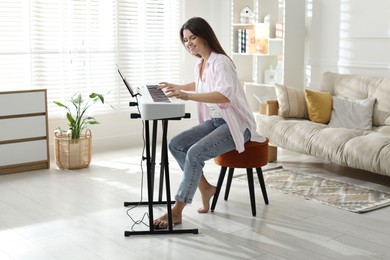 Smiling woman playing synthesizer at home. Electronic musical instrument