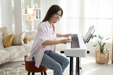 Photo of Smiling woman playing synthesizer at home. Electronic musical instrument