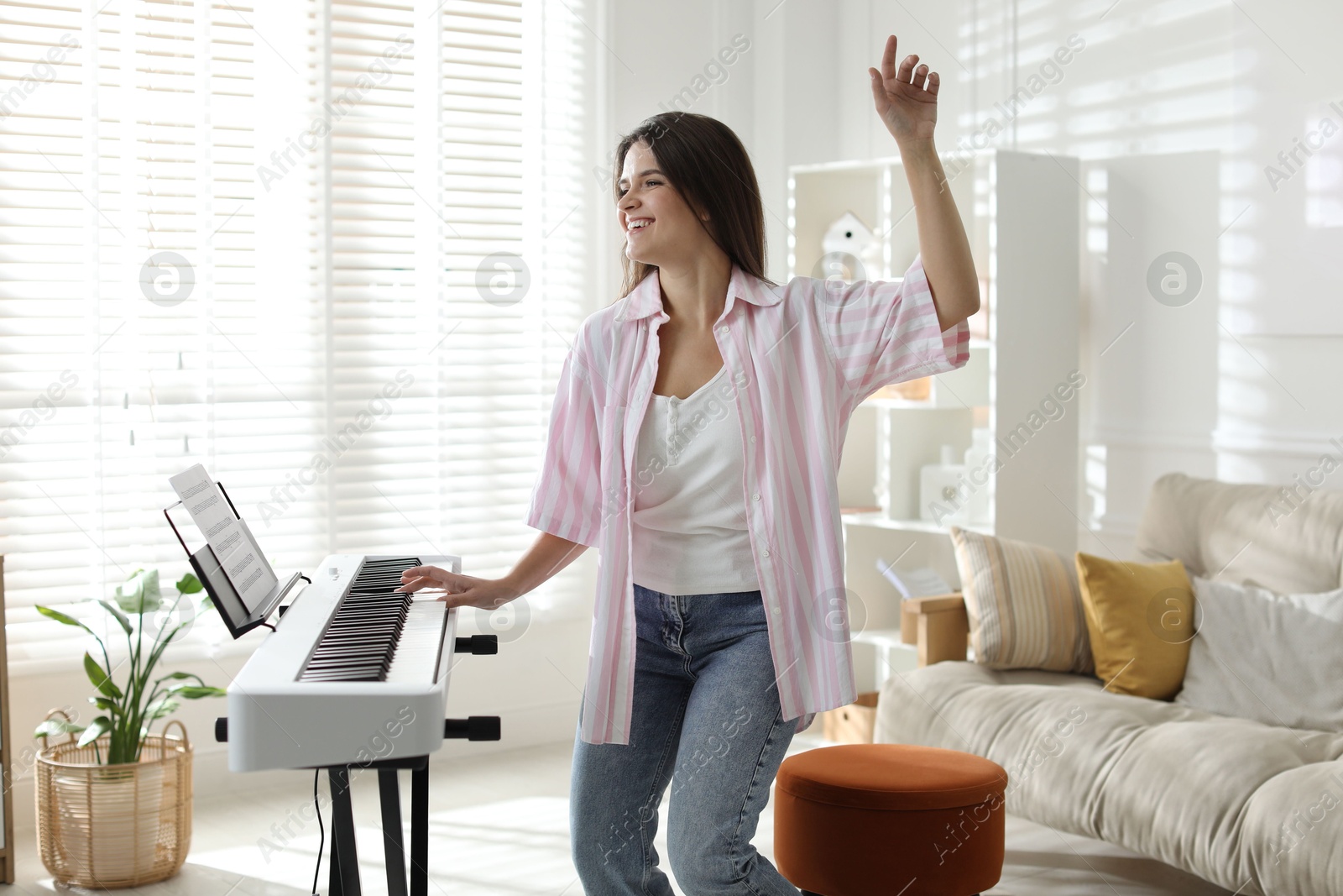 Photo of Smiling woman playing synthesizer and dancing at home