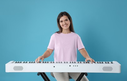 Photo of Smiling woman playing synthesizer on light blue background