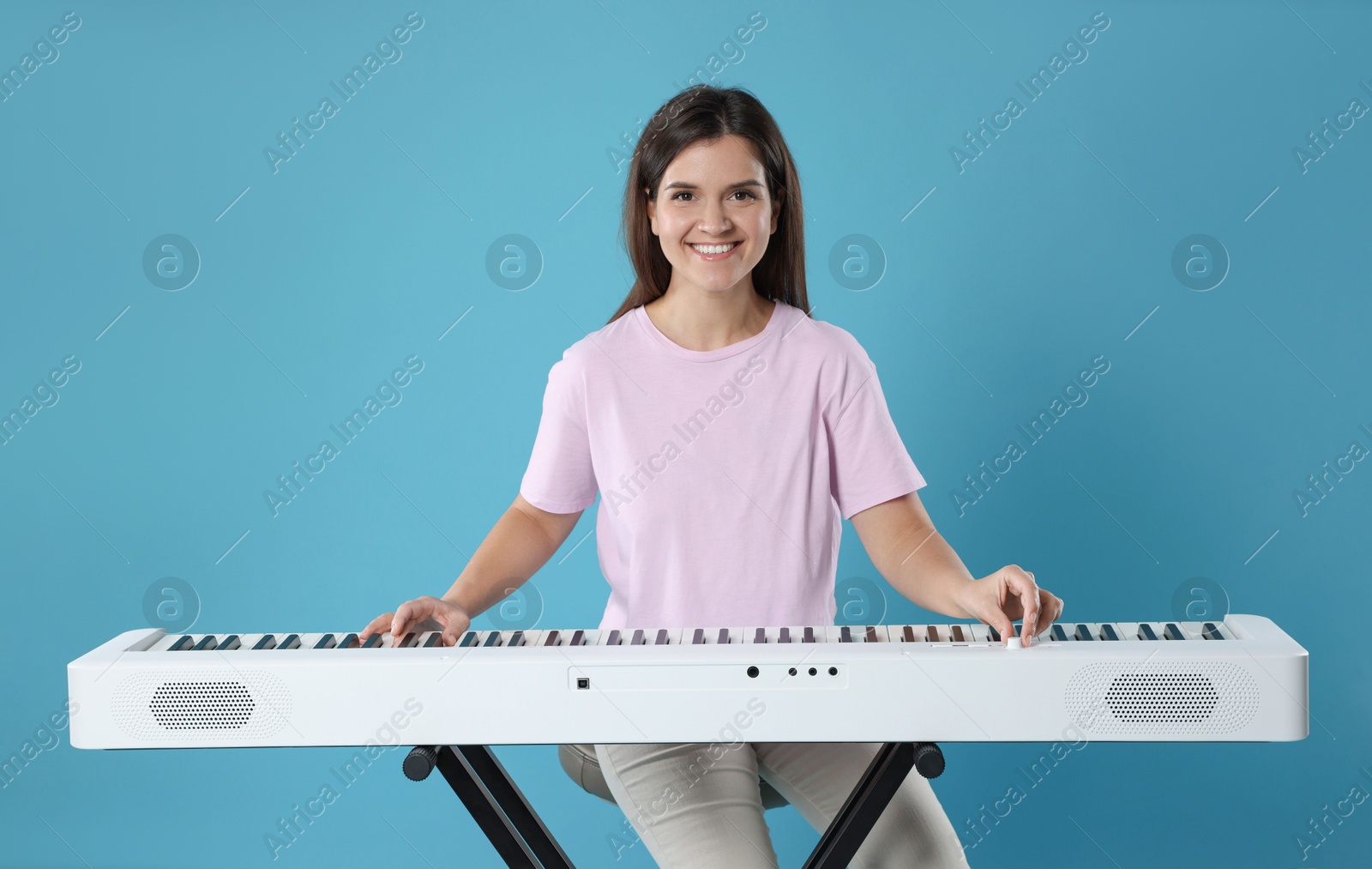 Photo of Smiling woman playing synthesizer on light blue background