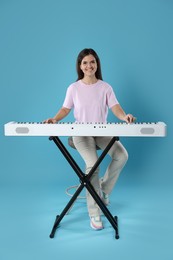 Photo of Smiling woman playing synthesizer on light blue background