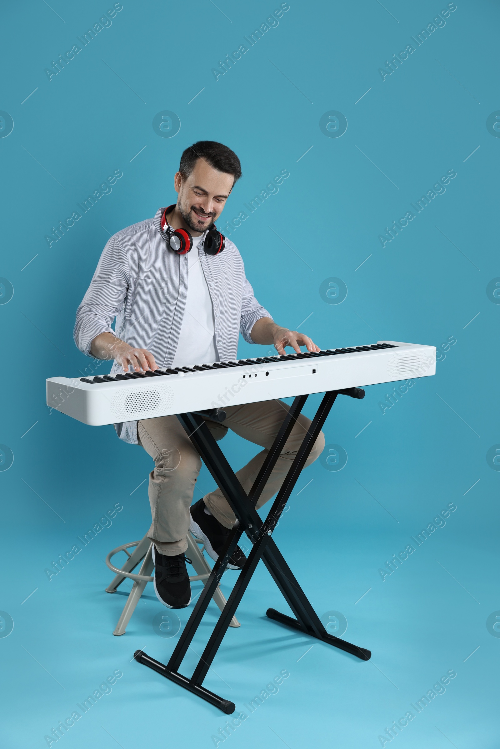 Photo of Smiling man playing synthesizer on light blue background