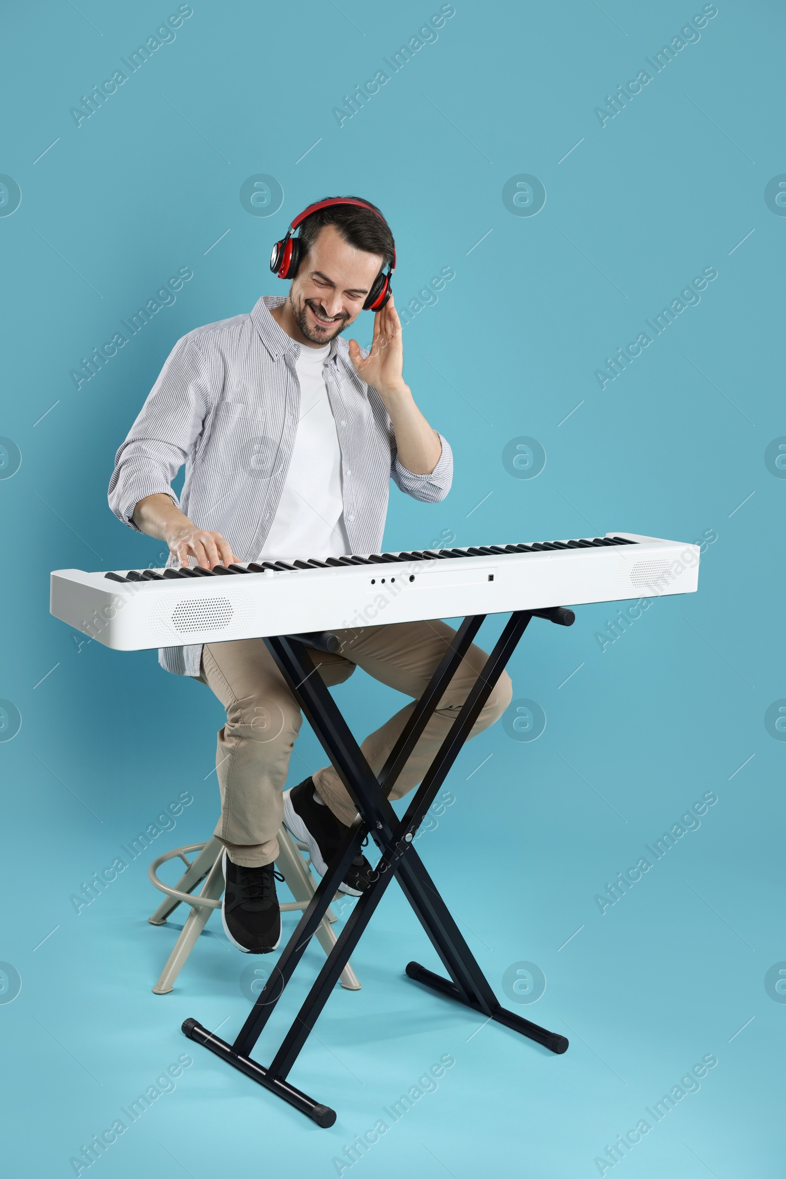 Photo of Smiling man playing synthesizer on light blue background