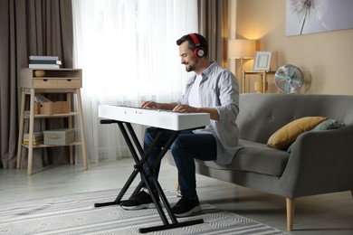 Photo of Smiling man in headphones playing synthesizer at home