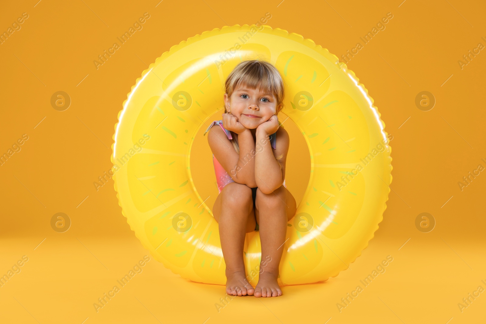 Photo of Cute little girl in swimsuit with inflatable ring and on orange background