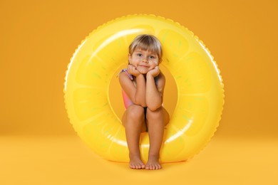 Photo of Cute little girl in swimsuit with inflatable ring and on orange background