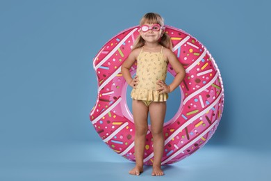 Photo of Cute little girl in swimsuit with inflatable ring and swim goggles on light blue background