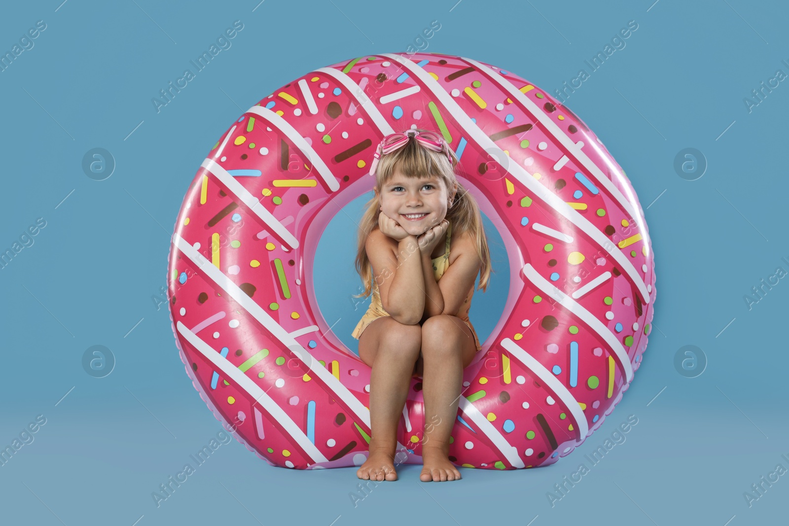 Photo of Cute little girl in swimsuit with inflatable ring and swim goggles on light blue background