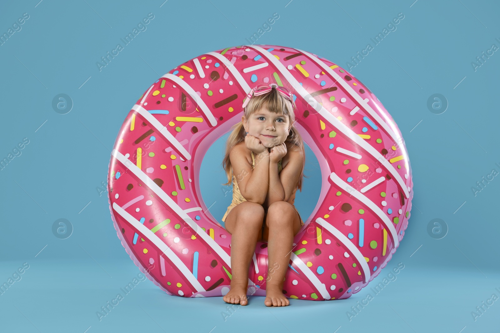 Photo of Cute little girl in swimsuit with inflatable ring and swim goggles on light blue background