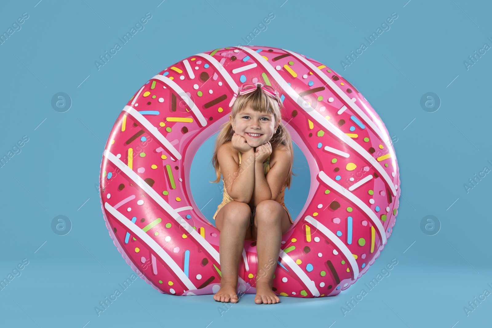 Photo of Cute little girl in swimsuit with inflatable ring and swim goggles on light blue background