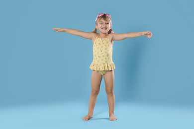 Photo of Cute little girl in swimsuit with swim goggles on light blue background