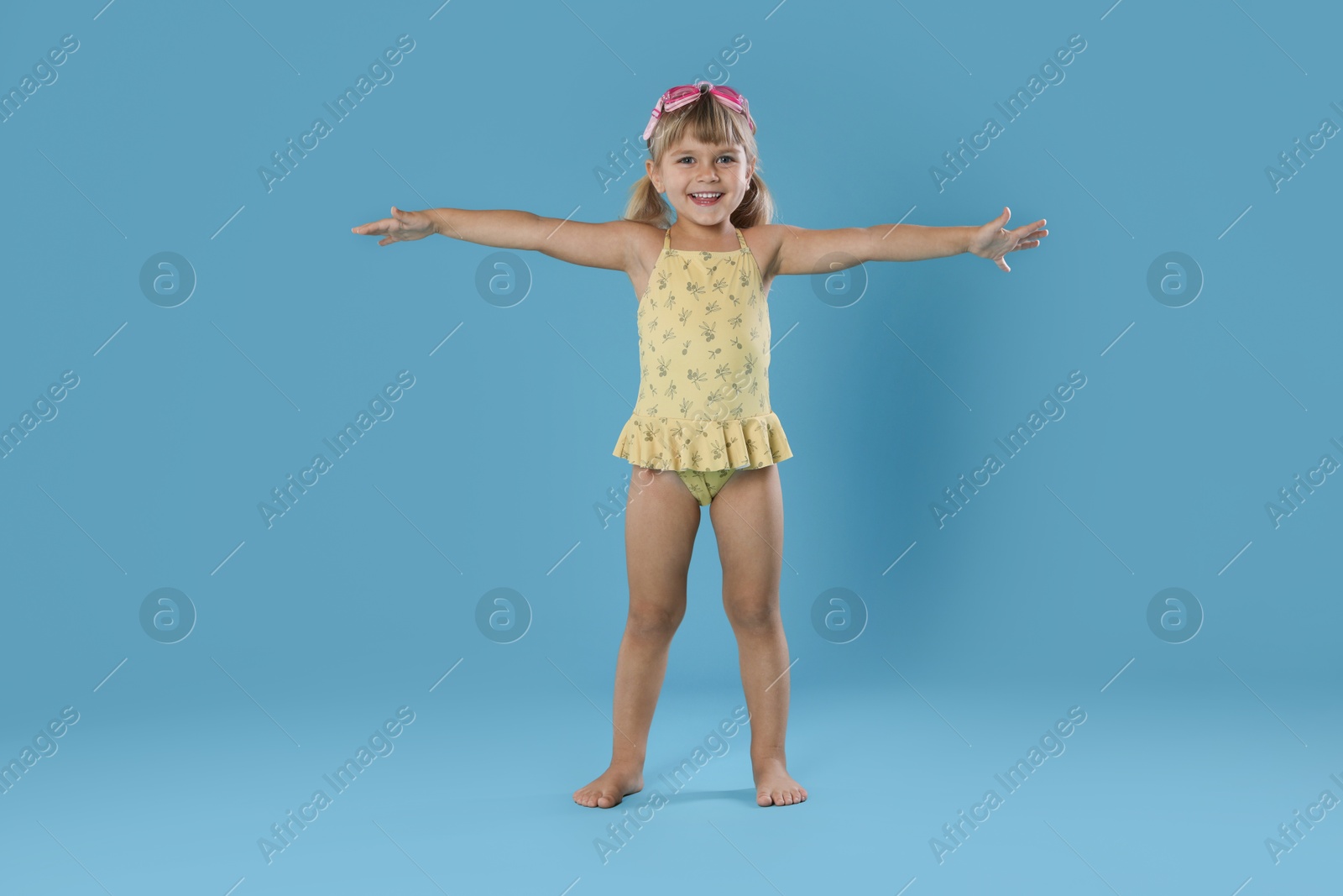 Photo of Cute little girl in swimsuit with swim goggles on light blue background