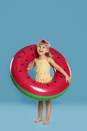 Photo of Cute little girl in swimsuit with inflatable ring and swim goggles on light blue background