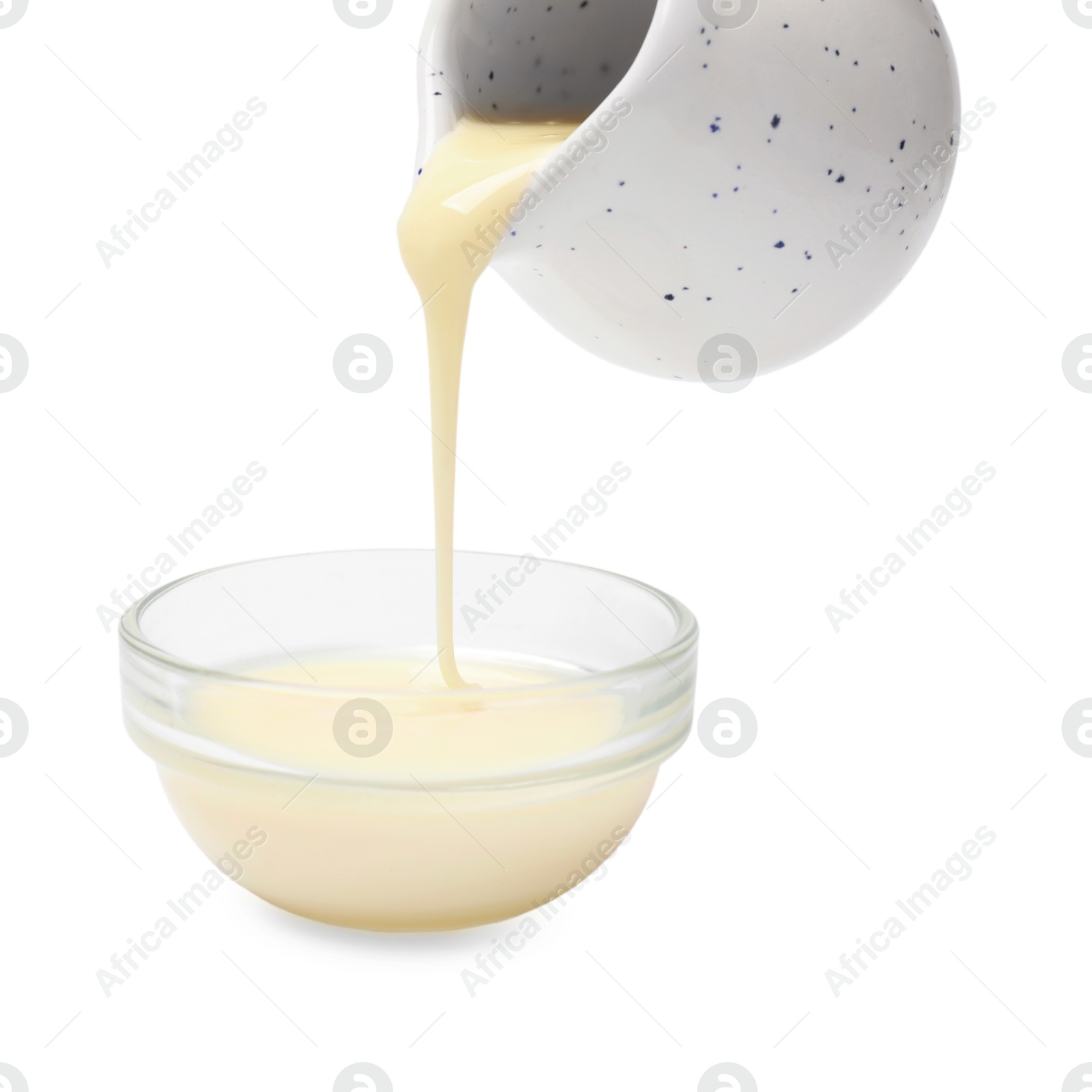 Photo of Pouring delicious condensed milk from jug into bowl isolated on white