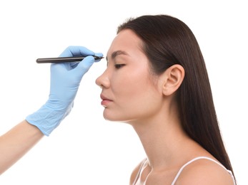 Doctor drawing marks on patient's nose for plastic surgery operation against white background, closeup