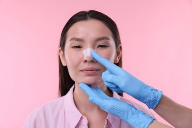 Photo of Doctor checking patient's nose after plastic surgery operation on pink background, closeup