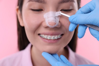 Photo of Doctor removing medical bandage from patient's nose after plastic surgery operation on pink background, closeup