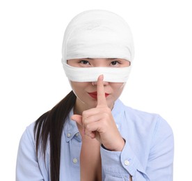 Photo of Woman with nose wrapped in medical bandage after plastic surgery operation making silent gesture on white background