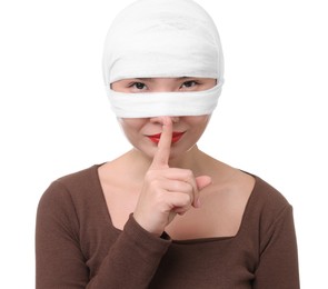 Photo of Woman with nose wrapped in medical bandage after plastic surgery operation making silent gesture on white background