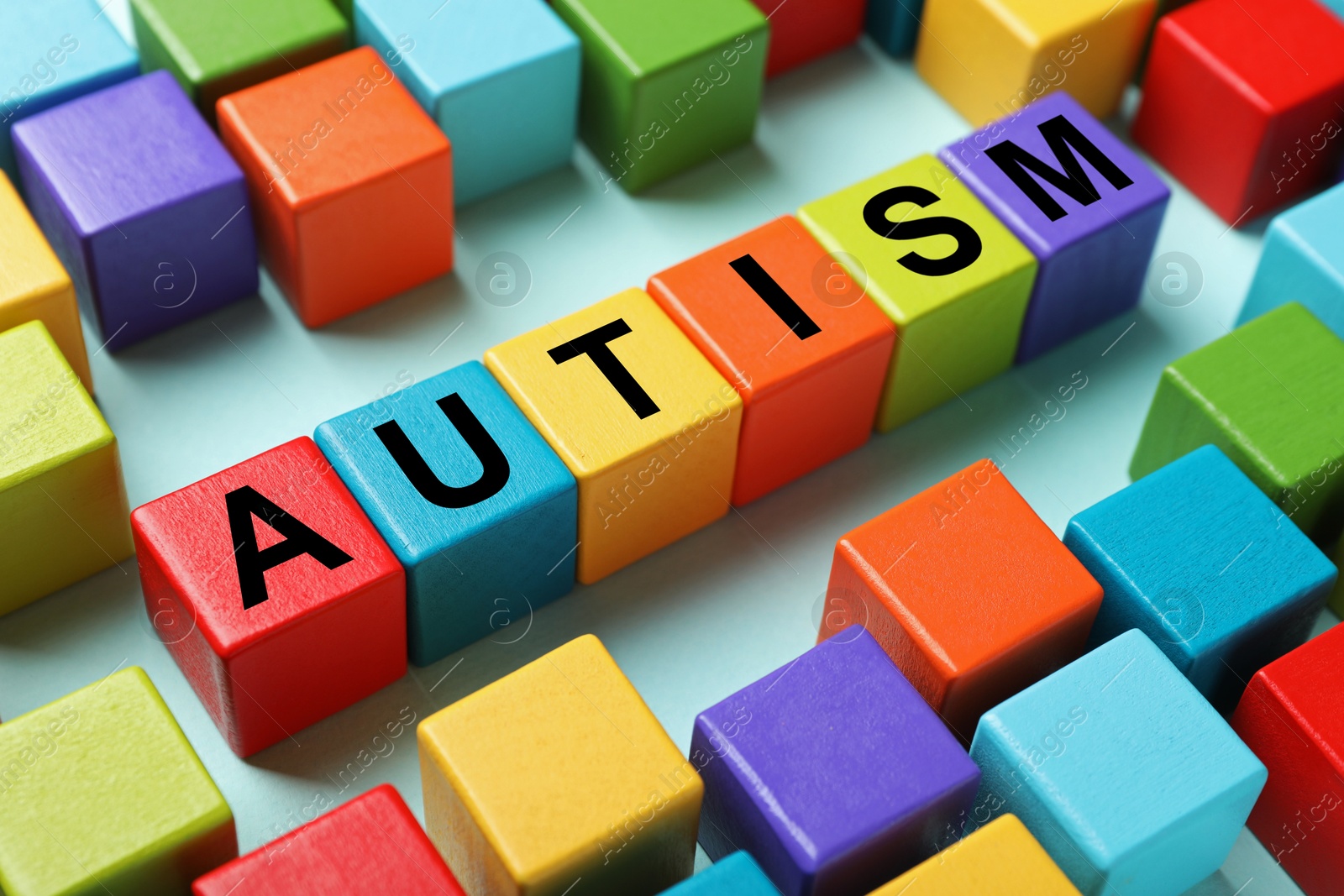 Photo of Word Autism made with colorful cubes on light blue background, closeup