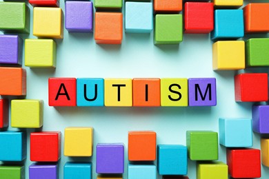 Photo of Word Autism made with colorful cubes on light blue background, flat lay